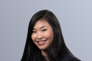Young woman with long dark hair smiling in front of a gray background.
