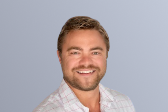 "Smiling man with short hair and beard wearing a light plaid shirt against a plain background."