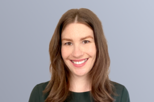 Portrait of a smiling person with brown hair, wearing a green top, against a plain gray background.