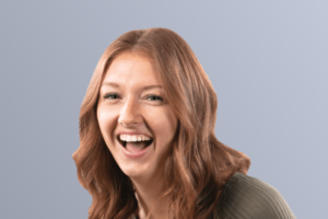 Smiling woman with red hair and a green top against a light blue background.