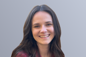 Smiling woman with long dark hair wearing a maroon top against a gray background.