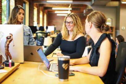 People collaborating in a modern office environment with laptops and desktop computers.