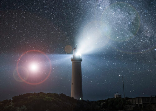 "Lighthouse illuminating under a starry night sky with the Milky Way visible in the background."