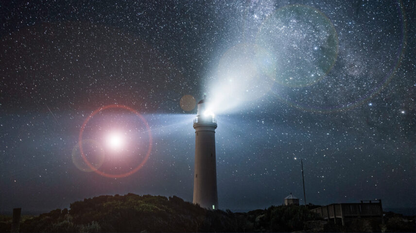 "Lighthouse illuminating under a starry night sky with the Milky Way visible in the background."