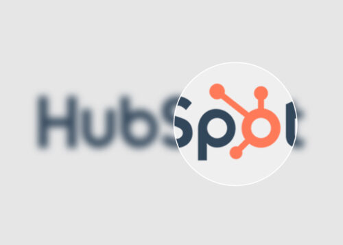 "HubSpot logo magnified, showcasing the orange sprocket design and partial company name against a blurred background."