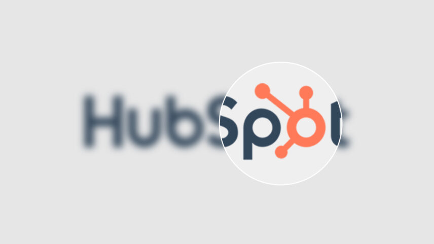 "HubSpot logo magnified, showcasing the orange sprocket design and partial company name against a blurred background."