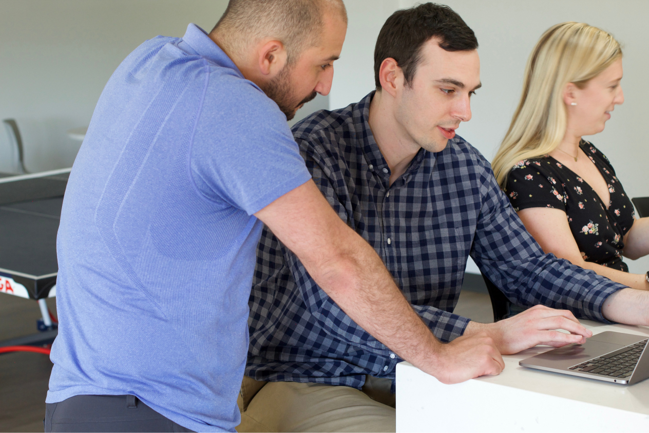 Three colleagues collaborating on a project around a laptop with a ping pong table in the background.