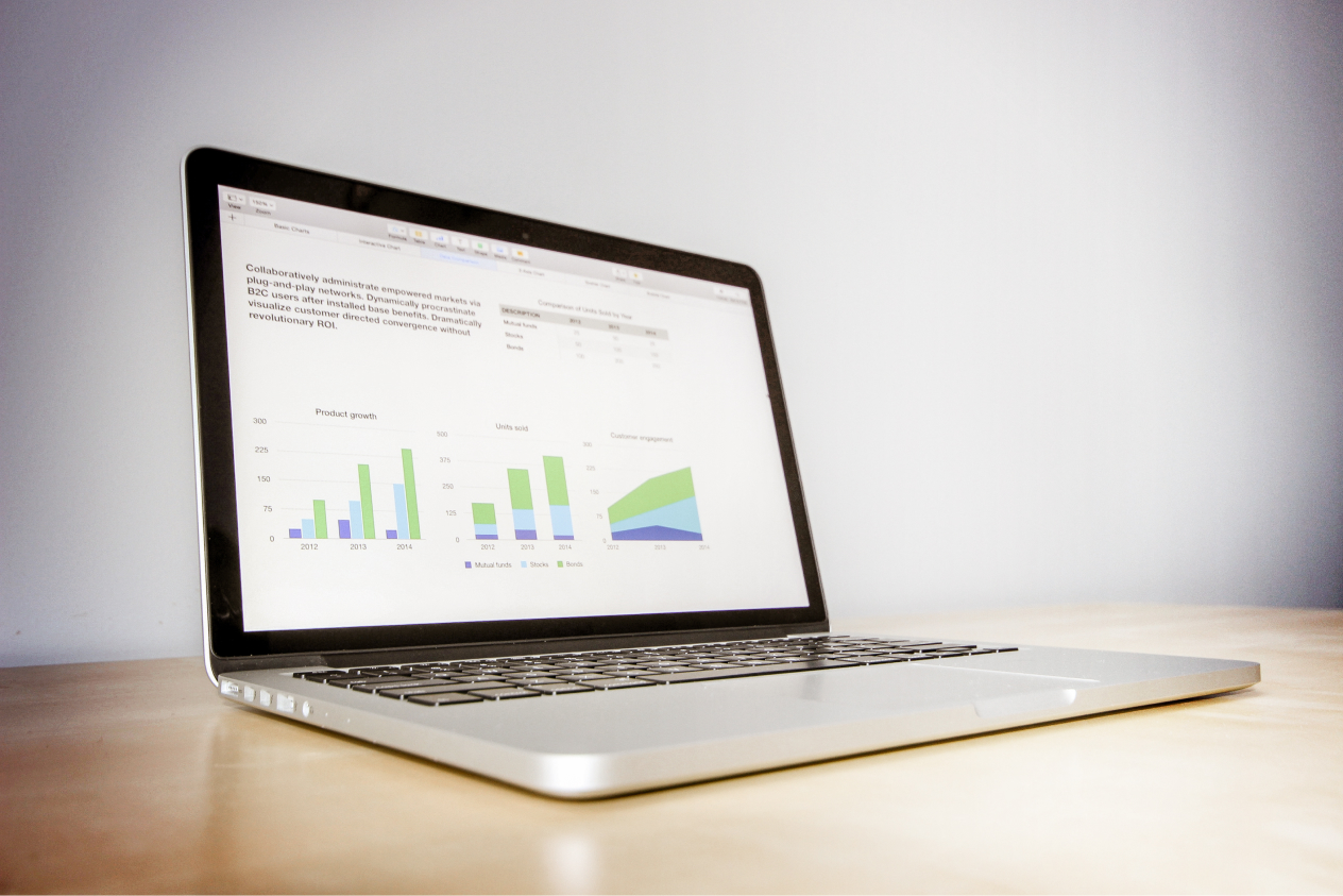 Laptop displaying business analytics graphs on screen, placed on a light wooden desk against a plain background.