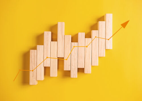 Wooden blocks arranged in a staggered upward pattern with an orange arrow indicating growth on a yellow background.