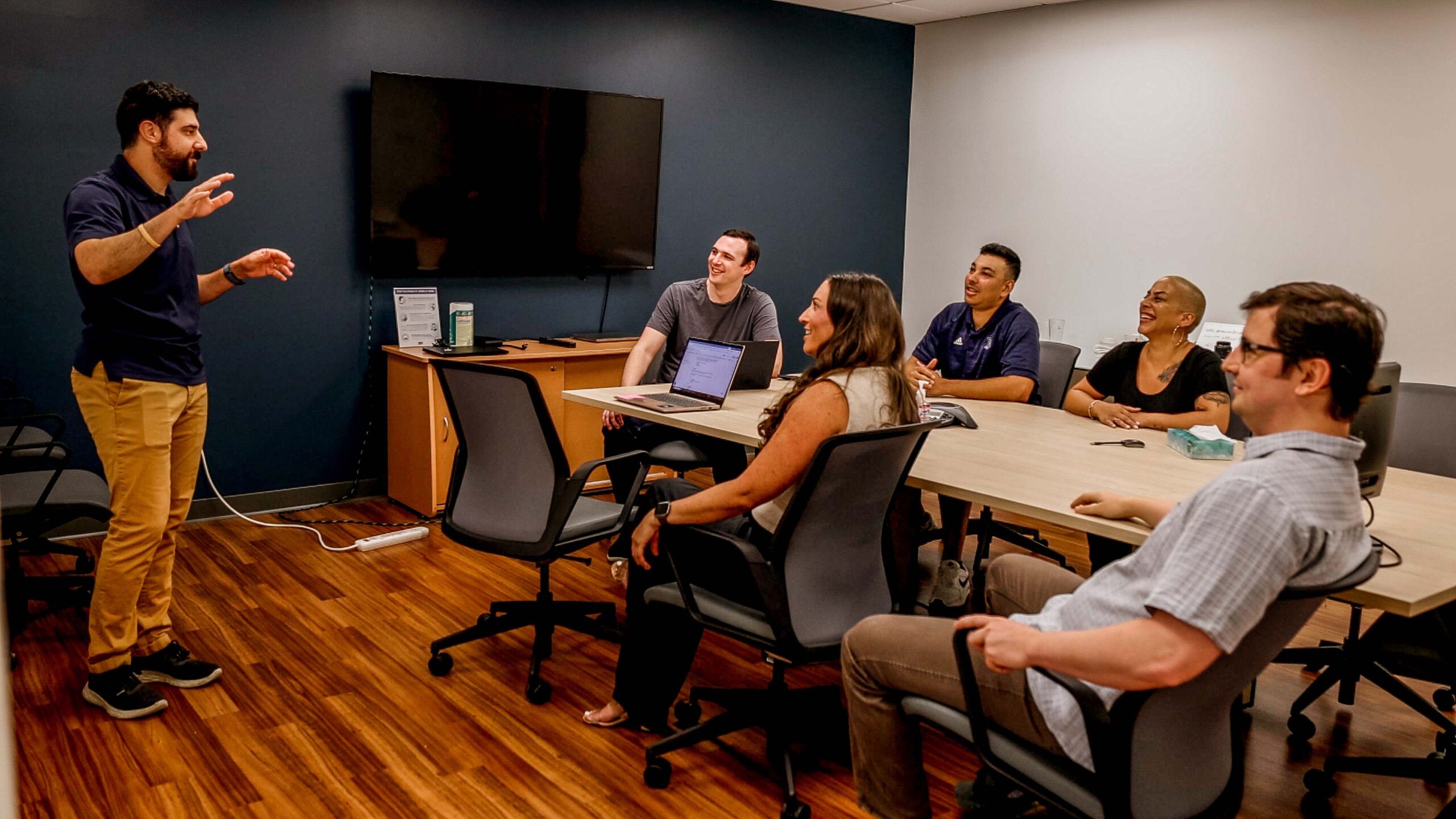 A man giving a presentation to a group of people seated around a conference table in an office setting.