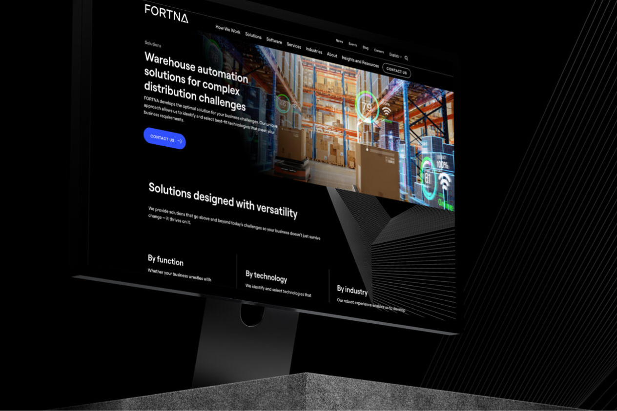 Monitor displaying a warehouse automation solutions website with images of a warehouse and boxes.