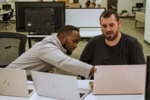 Two men collaborating at a desk with laptops in a modern office space.