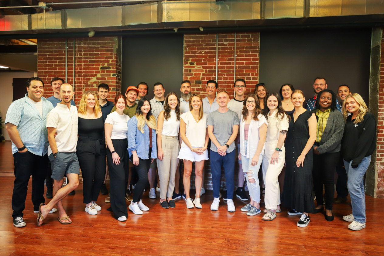 Group of employees posing for a photo in a modern office space with brick walls and wooden floors