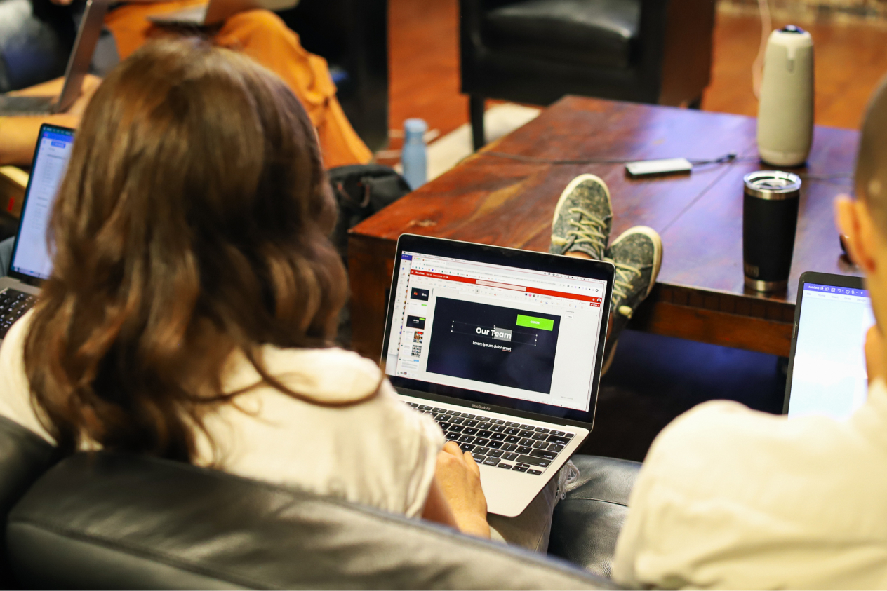 People working on laptops at a wooden table in a casual office environment.
