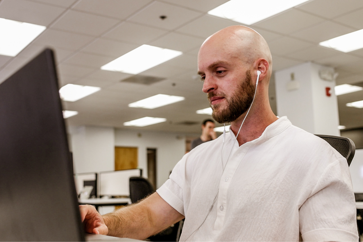 Man wearing earphones working on a laptop in an office setting.