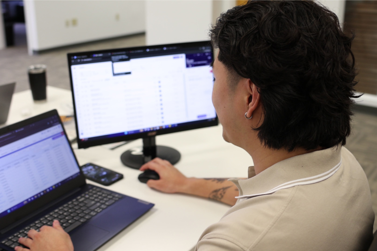 Person working on computers at a desk in an office, looking at data on screens