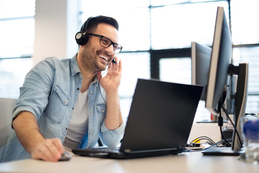Outsourced sales development rep on video call using headset and laptop in a modern office.