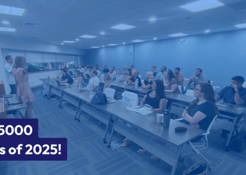 Indoor classroom setting with a group of people seated at tables listening to a presentation with a "Class of 2025" sign.